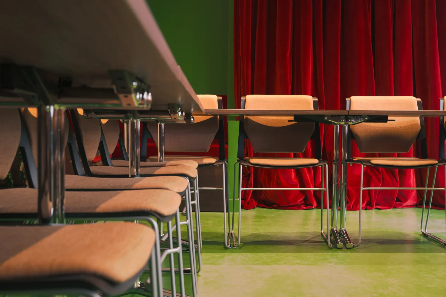 Les chaises alignées le long de la table, vues à hauteur d'assise, devant le velours rouge.