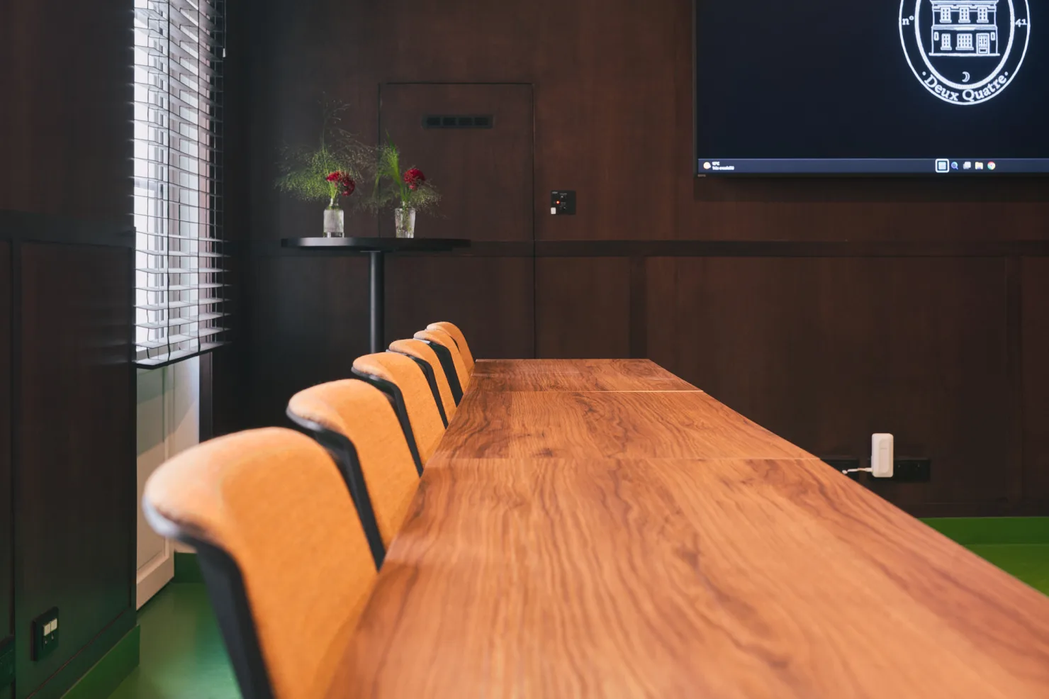 Le bout d'une longue table de bois, les chaises alignées, l'écran dans l'angle.