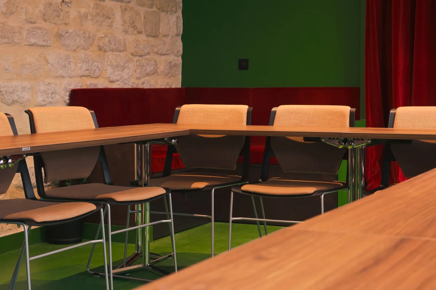 Un angle de la table en U, la banquette rouge et le mur de pierre derrière les chaises.